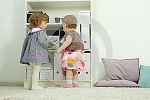 Two happy little girls stand near shelves and look