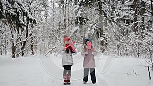 Two happy little girls stand in a snowy forest in winter