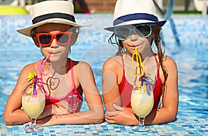 Two happy little girls in sunglasses with cocktails wearing hats