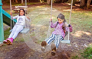 Two happy little girls swinging on the swing in a childrens playground