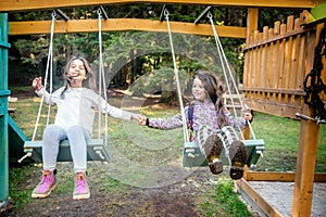 Two happy little girls swinging on the swing