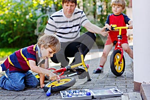 Two happy little kid boys and father repair chain on bikes and change wheel of balance bicycle