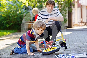 Two happy little kid boys and father repair chain on bikes and change wheel of balance bicycle