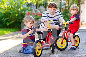 Two happy little kid boys and father repair chain on bikes and change wheel of balance bicycle