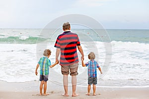 Two happy little kids boys and father standing on the beach of ocean and looking on horizon on stormy day. Family, dad