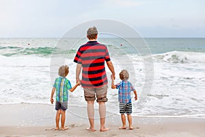Two happy little kids boys and father standing on the beach of ocean and looking on horizon on stormy day. Family, dad