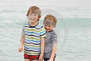 Two happy little kids boys running on the beach of ocean. Funny children, siblings, twins and best friends making