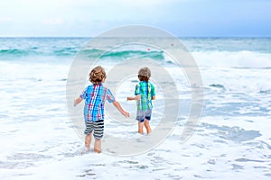 Two happy little kids boys running on the beach of ocean. Funny cute children, sibling and best friends making vacations