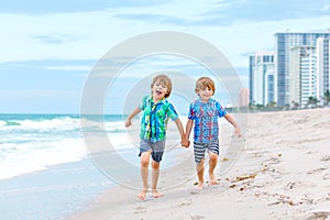 Two happy little kids boys running on the beach of ocean. Funny cute children, sibling and best friends making vacations