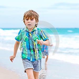 Two happy little kids boys running on the beach of ocean. Funny cute children, sibling and best friends making vacations