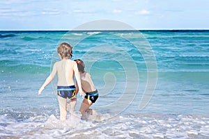 Two happy little kids boys running on the beach of ocean. Funny cute children, siblings, twins and best friends making