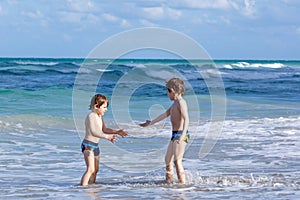 Two happy little kids boys running on the beach of ocean. Funny cute children, siblings, twins and best friends making