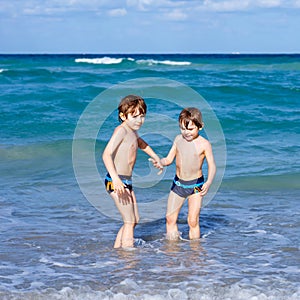 Two happy little kids boys running on the beach of ocean. Funny cute children, siblings, twins and best friends making