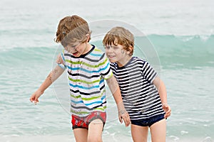 Two happy little kids boys running on the beach of ocean