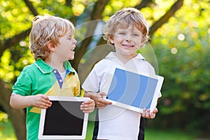 Two happy little sibling kids holding tablet pc, outdoors