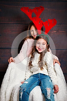 Two happy little smiling girls embracing .Christmas concept. Smiling funny sisters in deer horns in studio.