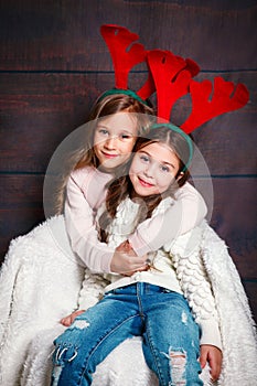 Two happy little smiling girls embracing .Christmas concept. Smiling funny sisters in deer horns in studio.