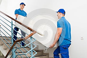 Two Male Movers Carrying Sofa On Staircase