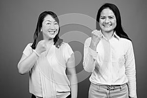 Two happy mature Asian businesswomen smiling together in studio