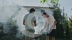 Two happy men cooking grilling bacon and sausages on grid