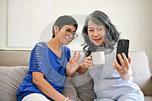 Two happy middle-aged Asian women talking with their grandchild through a video call