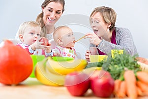 Two happy mothers and best friends smiling while feeding their babies