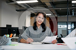 Two happy multiracial businesswomen smiling while reviewing documents during meeting in office