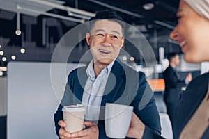 Two happy multiracial colleagues talking and drinking coffee during break time in office