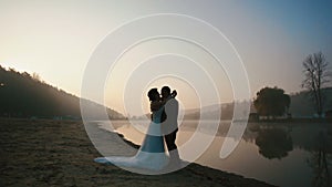 Two happy newlyweds have sweet talk and kissing at the evening of wedding day at the romantic lake on the sunset