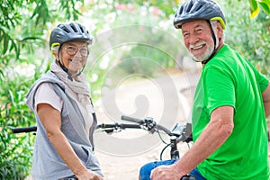 Two happy old mature people enjoying and riding bikes together to be fit and healthy outdoors. Active seniors having fun training