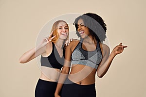 Two happy pretty diverse girls wearing sportswear having fun on beige background.