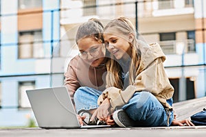 Two happy schoolgirls in casualwear looking at laptop screen