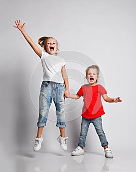 Two happy screaming kid girls in jeans sisters playing jumping with hands up. Happiness, childhood, freedom, movement