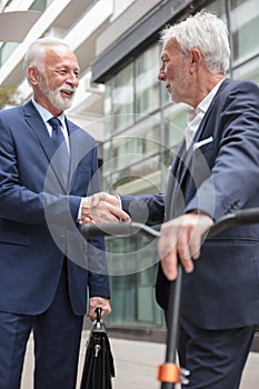 Two happy senior businessmen shaking hands, standing in front of an office building