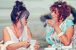 Two happy senior women talking and drinking coffee  in a outdoor cafe