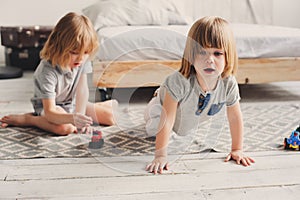 Two happy sibling boys playing together at home with toy cars