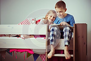 Two happy sibling children reading book in bunk bed