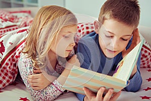 Two happy sibling children reading book in bunk bed under blanket