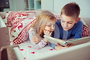 Two happy sibling children reading book in bunk bed under blanket