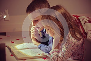 Two happy sibling children reading book in bunk bed under blanket