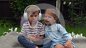 Two Happy Siblings boy ans girl listening to music on headphones outside in Garden. Children and technology. Brother and