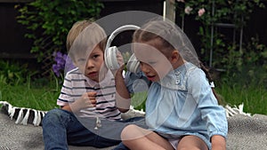 Two Happy Siblings boy ans girl listening to music on headphones outside in Garden. Children and technology. Brother and
