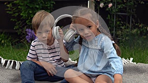 Two Happy Siblings boy ans girl listening to music on headphones outside in Garden. Children and technology. Brother and