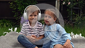 Two Happy Siblings boy ans girl listening to music on headphones outside in Garden. Children and technology. Brother and