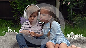 Two Happy Siblings boy ans girl listening to music on headphones outside in Garden. Children and technology. Brother and