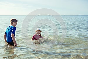 Two happy siblings children in neoprene swimingsuit  playing in sea