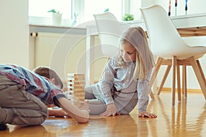 Two happy siblings playing a game with wooden blocks at home