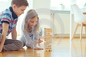 Two happy siblings playing a game with wooden blocks at home