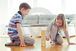 Two happy siblings playing a game with wooden blocks at home