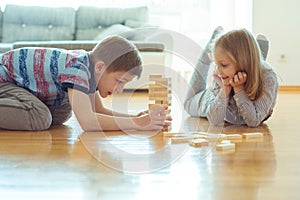 Two happy siblings playing a game with wooden blocks at home